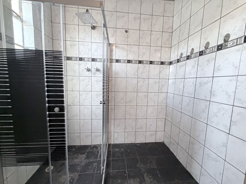 A walk-in shower area featuring marble-effect wall tiles, a dark tiled floor, and a glass shower enclosure.