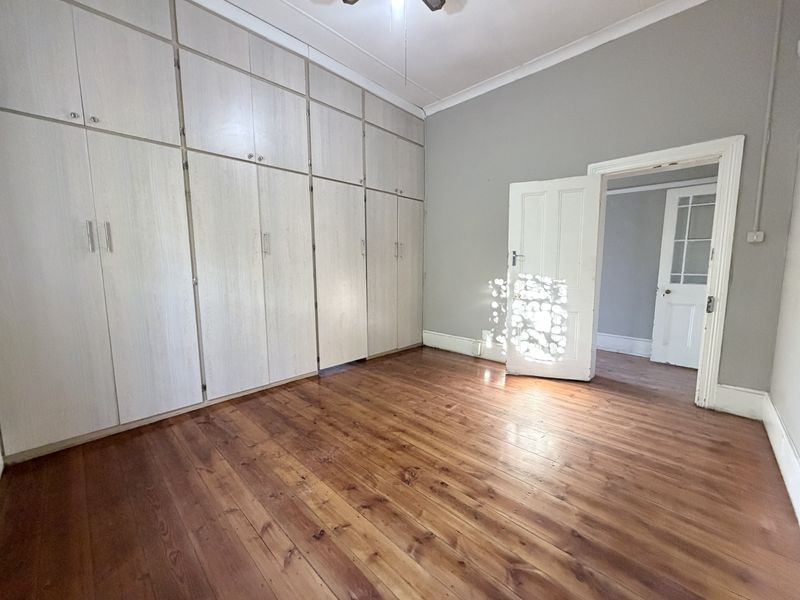A spacious, empty bedroom featuring polished timber flooring, extensive floor-to-ceiling built-in cupboards, and classic panelled doors leading to an adjacent room.