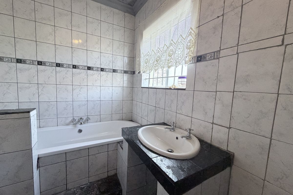 A dated bathroom featuring a built-in bathtub, tiled vanity with a drop-in basin, and full-height wall tiling.