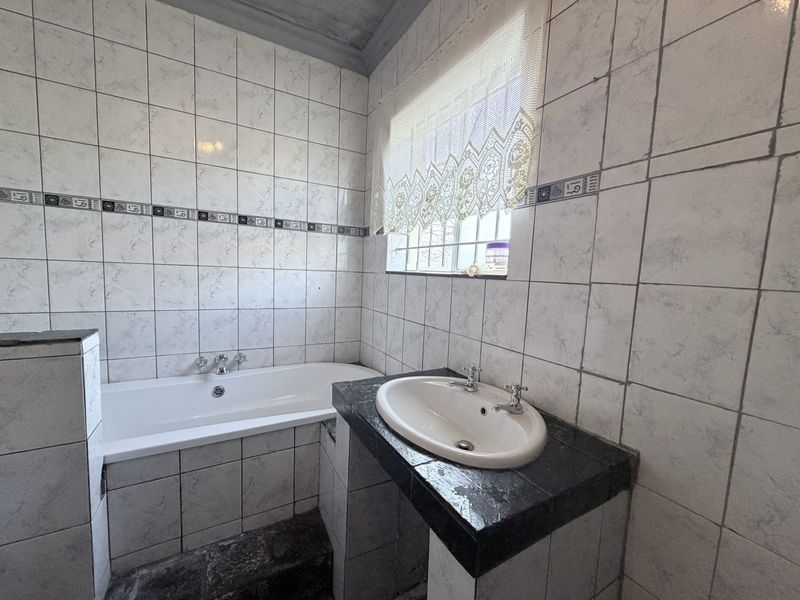 A dated bathroom featuring a built-in bathtub, tiled vanity with a drop-in basin, and full-height wall tiling.