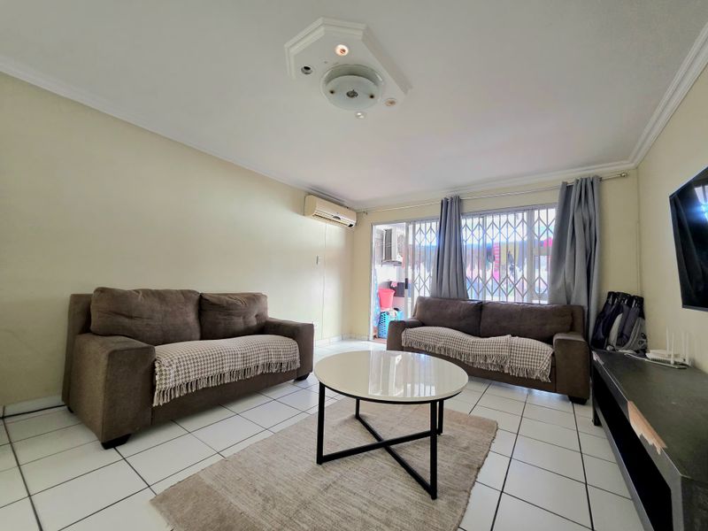 A functional living room featuring tiled flooring, a ceiling rose, and a wall-mounted air conditioning unit, with direct access to an outdoor area.