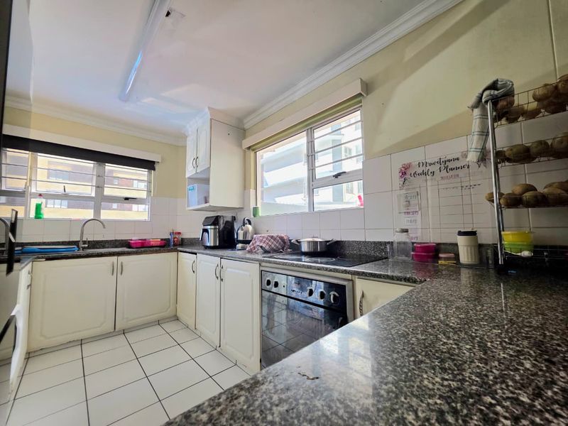 Functional kitchen featuring granite countertops, built-in oven, electric hob, and ample cabinetry with tiled flooring and backsplash.