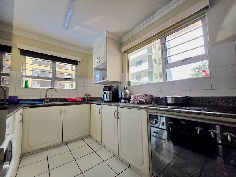 Functional kitchen featuring granite countertops, built-in cabinetry, electric hob, oven, and tiled flooring with ample natural light from louvered windows.