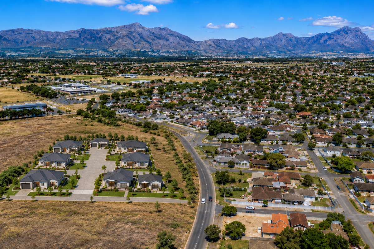 An aerial view of a residential neighborhood featuring a new housing development, paved roads, and scenic mountain views in the background.