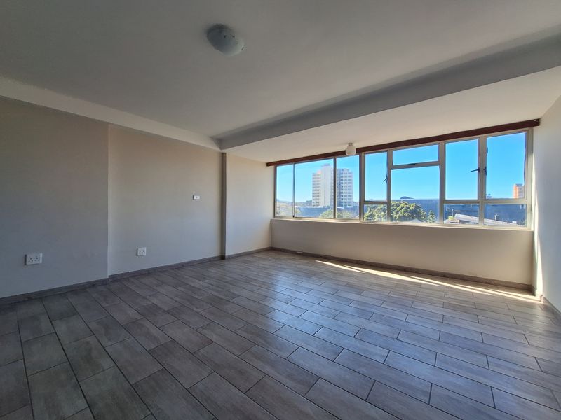 A bright and spacious empty living area featuring modern wood-look tiled flooring and large windows that provide ample natural light and urban views.
