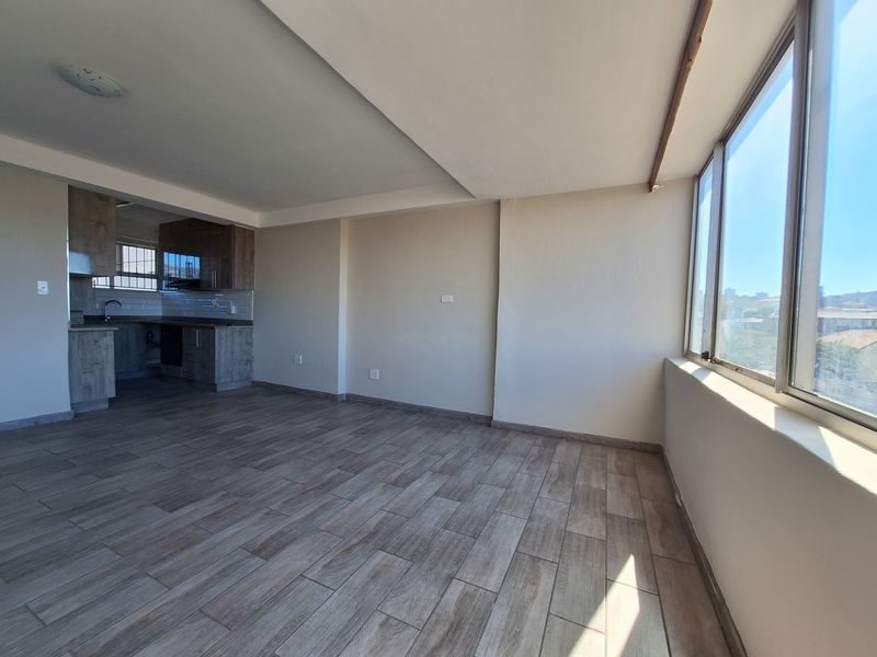 An open-plan living area featuring wood-look tile flooring, large windows for natural light, and an integrated kitchen with modern cabinetry.