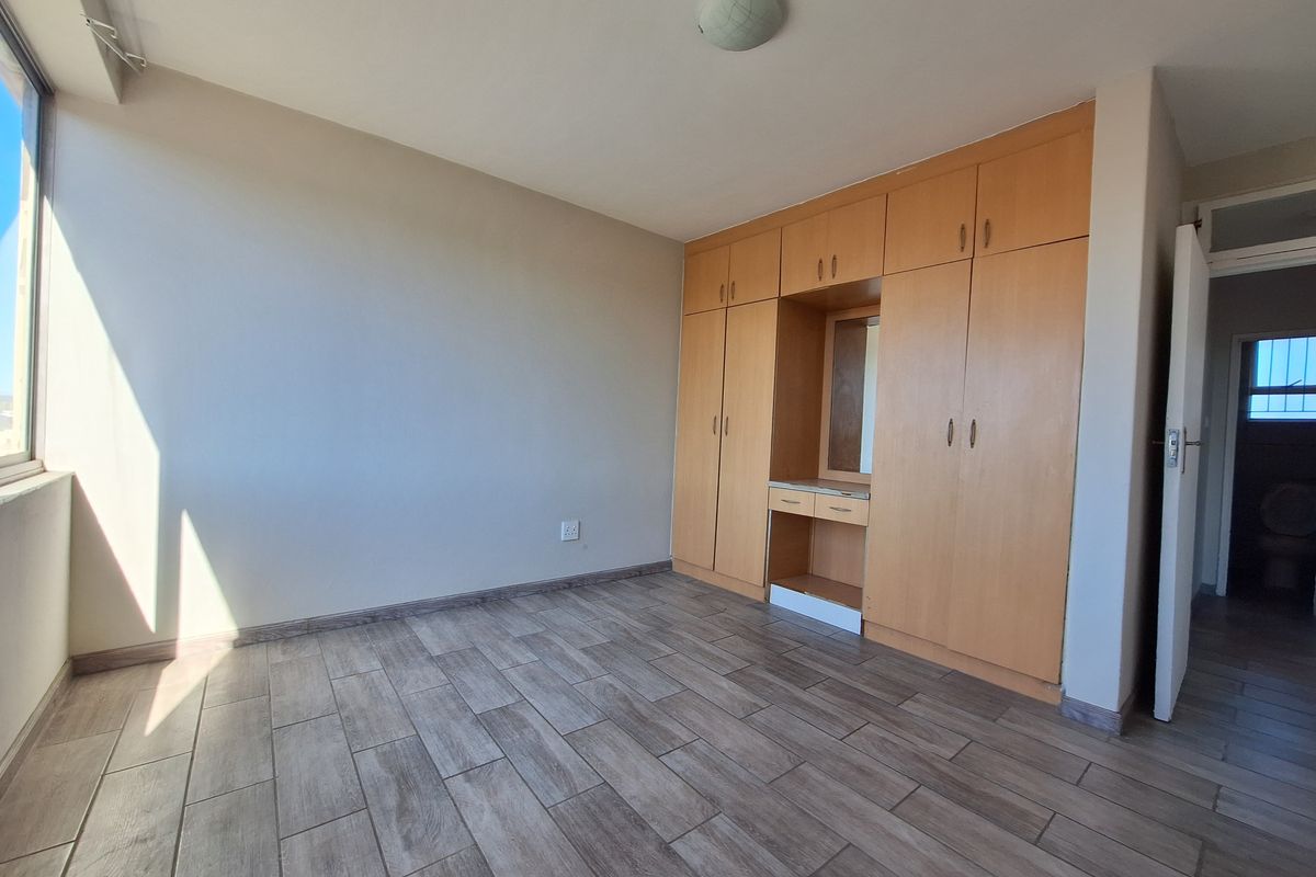 A bright, empty bedroom featuring modern wood-look tiled flooring and extensive built-in cabinetry with an integrated vanity area.