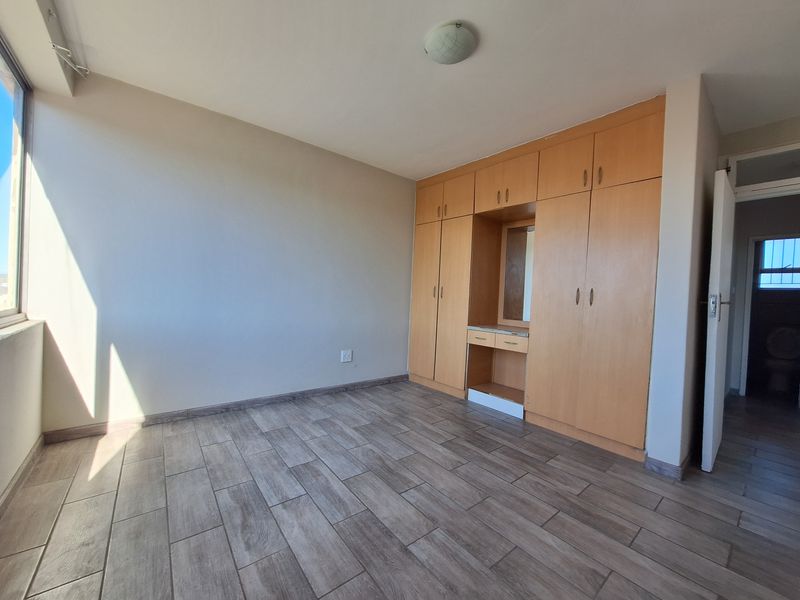 A bright, empty bedroom featuring modern wood-look tiled flooring and extensive built-in cabinetry with an integrated vanity area.