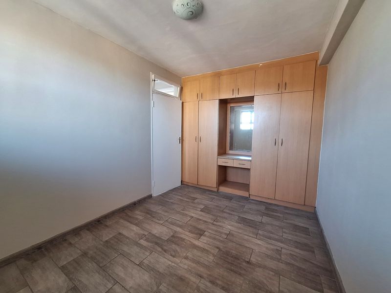 A clean, empty bedroom featuring modern wood-look tiled flooring and extensive built-in cabinetry with an integrated vanity mirror.