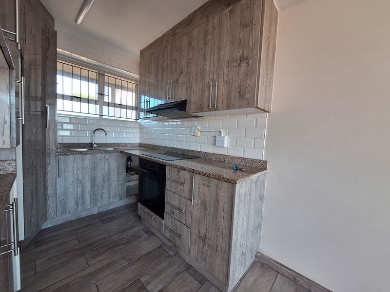 Modern kitchen featuring wood-grain cabinetry, granite countertops, subway tile backsplash, and integrated appliances including an oven, hob, and extractor fan.