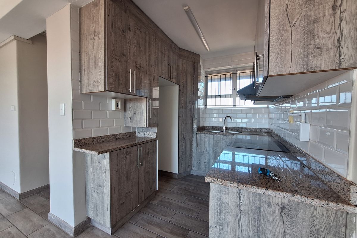 Modern kitchen featuring wood-look cabinetry, granite countertops, subway tile backsplash, built-in electric hob, extractor fan, and stainless steel sink.