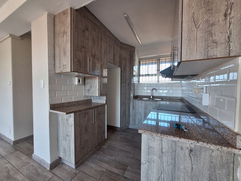 Modern kitchen featuring wood-look cabinetry, granite countertops, subway tile backsplash, built-in electric hob, extractor fan, and stainless steel sink.