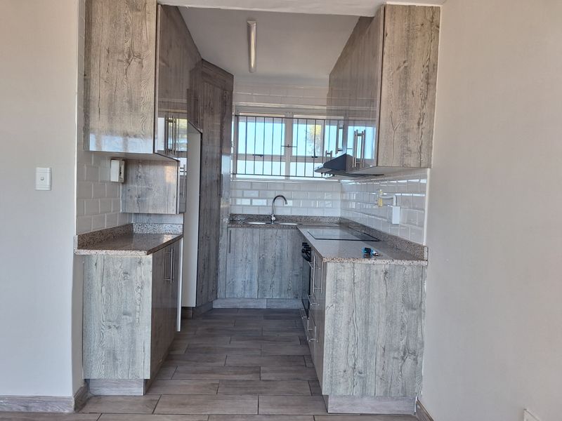 Modern galley-style kitchen featuring wood-look cabinetry, granite countertops, subway tile backsplash, and integrated cooking appliances.