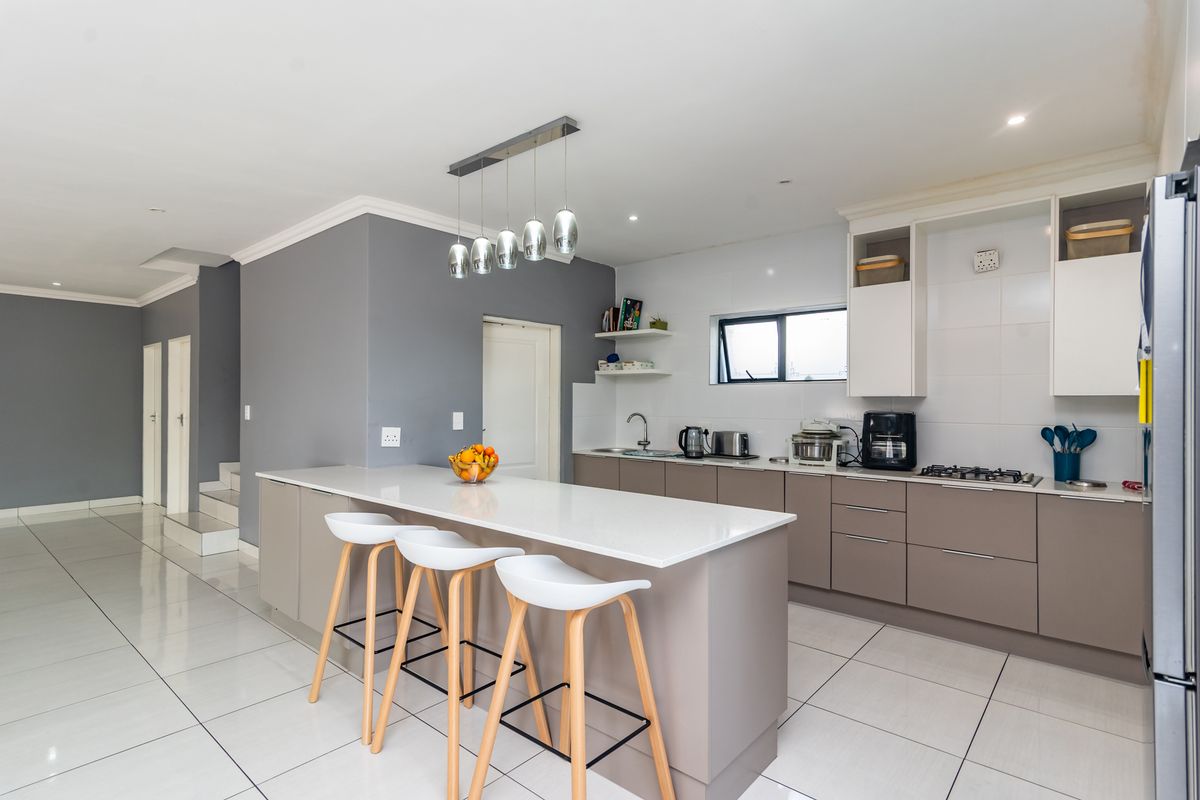 Modern kitchen featuring a central island with breakfast bar seating, sleek cabinetry, quartz countertops, and tiled flooring in an open-plan layout.