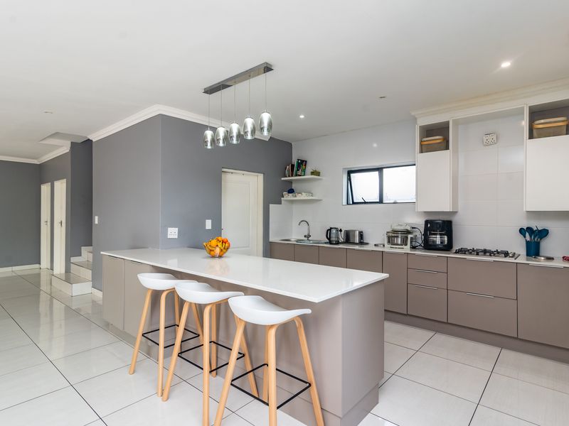 Modern kitchen featuring a central island with breakfast bar seating, sleek cabinetry, quartz countertops, and tiled flooring in an open-plan layout.