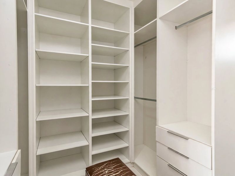 A clean and organized walk-in closet featuring extensive built-in shelving, hanging rails, and integrated storage drawers.