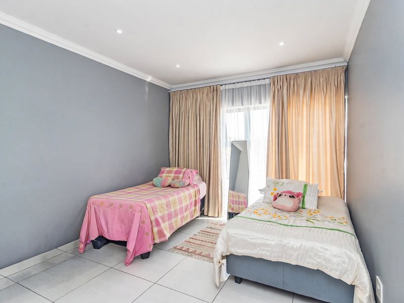 A well-lit bedroom featuring neutral grey walls, tiled flooring, recessed downlighting, and a sliding glass door providing access to the exterior.