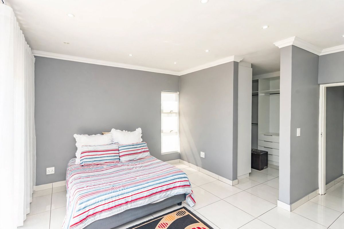 A well-maintained bedroom featuring neutral grey walls, tiled flooring, recessed downlighting, and a dedicated walk-in closet area with built-in cabinetry.