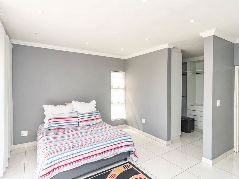 A well-maintained bedroom featuring neutral grey walls, tiled flooring, recessed downlighting, and a dedicated walk-in closet area with built-in cabinetry.