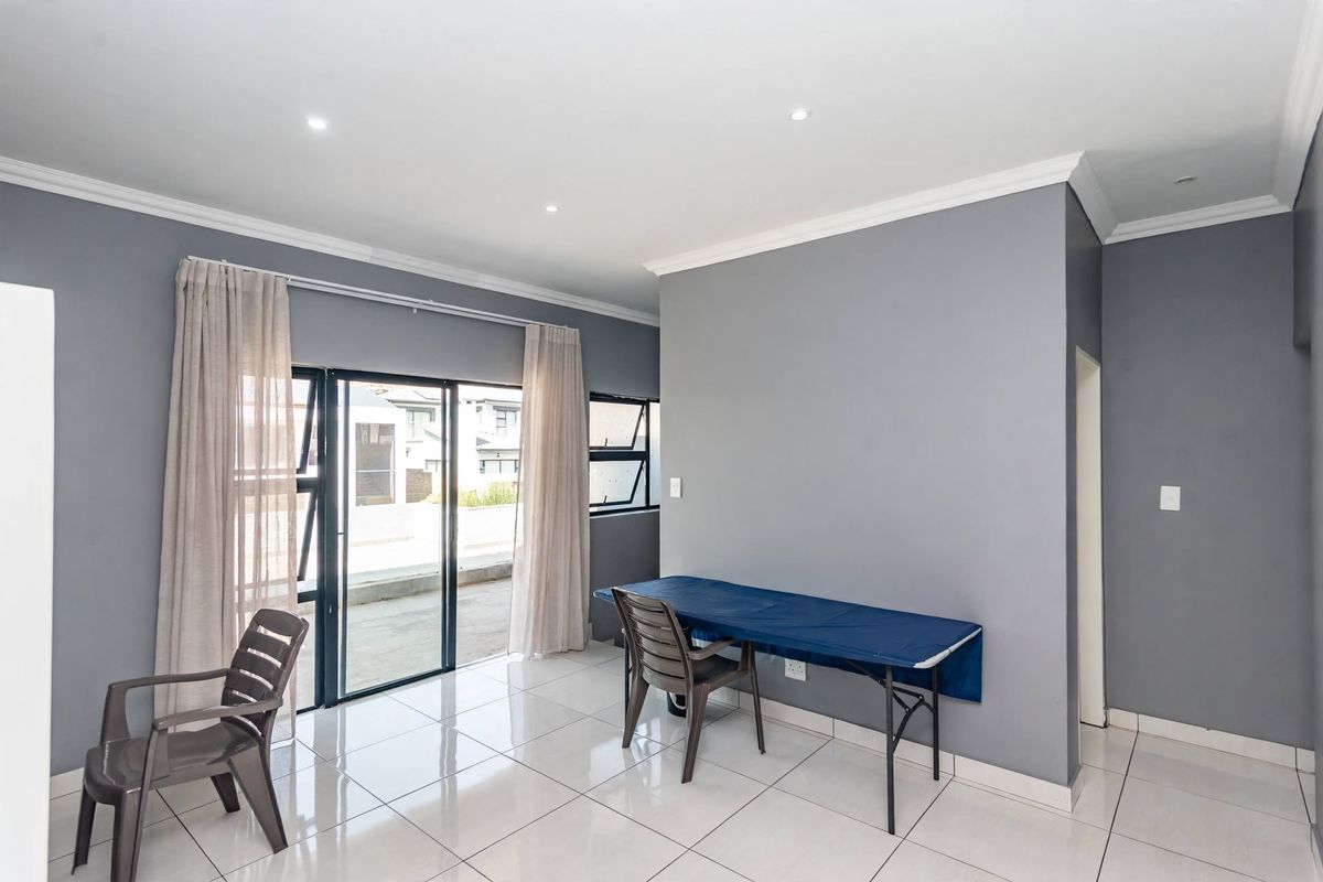 A bright, open-plan living area featuring neutral grey walls, polished tiled flooring, recessed lighting, and sliding glass doors leading to an outdoor space.