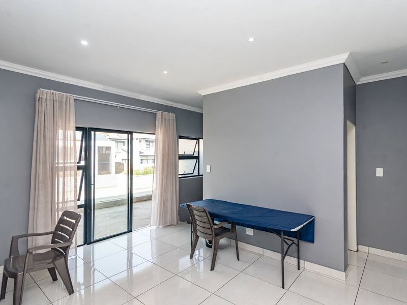 A bright, open-plan living area featuring neutral grey walls, polished tiled flooring, recessed lighting, and sliding glass doors leading to an outdoor space.