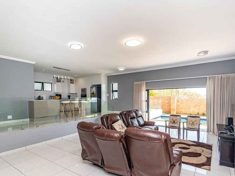 Spacious open-plan living area featuring modern tiled floors, a sleek kitchen with built-in cabinetry, and seamless access to the outdoor pool area.