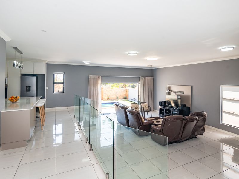 Spacious open-plan living area featuring a modern kitchen island, sleek tiled flooring, glass balustrade, and seamless flow to the outdoor pool area.