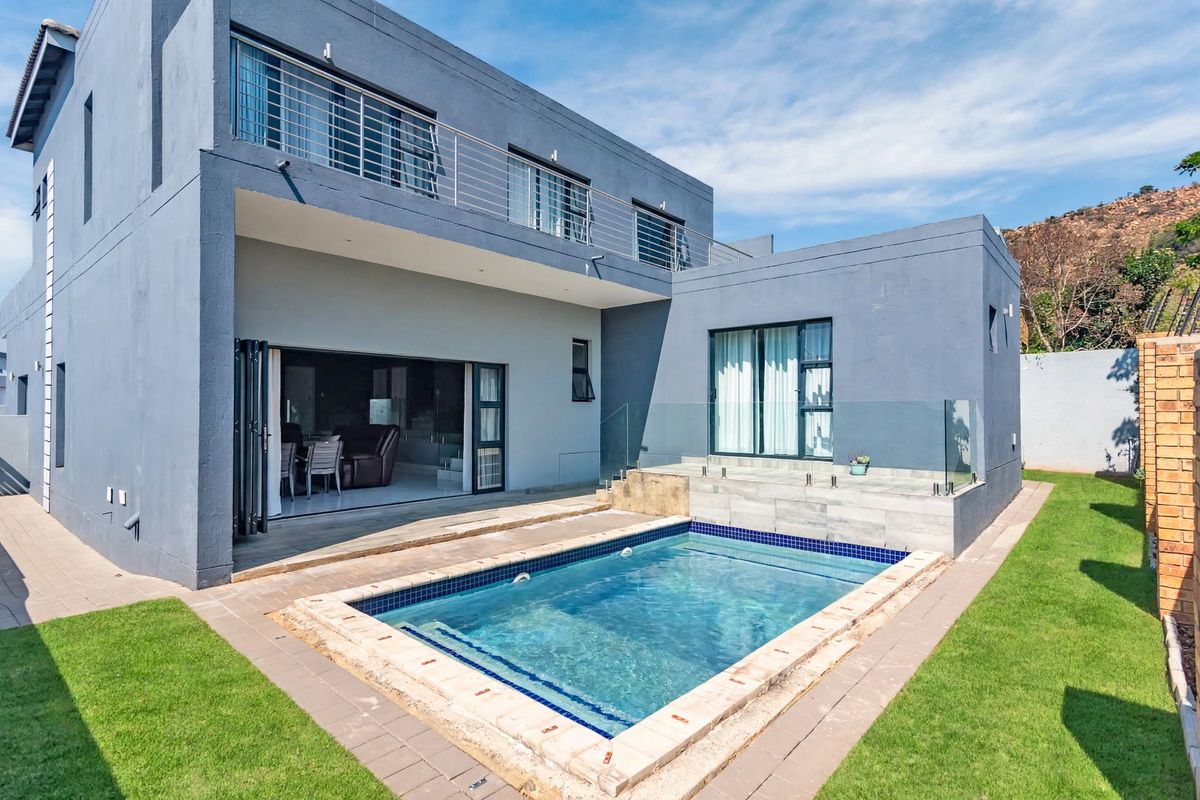 Rear exterior view featuring a swimming pool, glass balustrade, paved patio area, and large folding doors leading into the home.