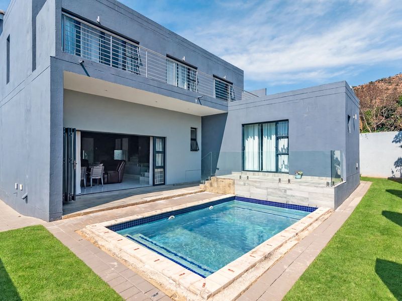 Rear exterior view featuring a swimming pool, glass balustrade, paved patio area, and large folding doors leading into the home.