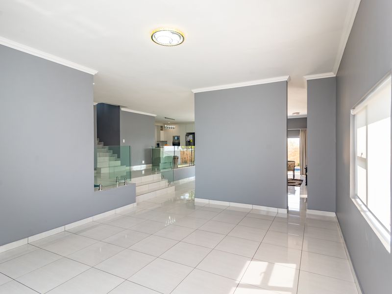 Spacious open-plan living area featuring neutral grey walls, polished tiled flooring, and a modern glass-railed staircase leading to the upper level.