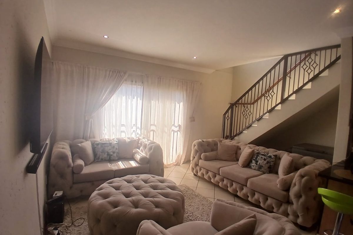 Spacious living room featuring tiled flooring, recessed downlights, and a staircase with a decorative metal balustrade, leading to a bright sliding glass door.