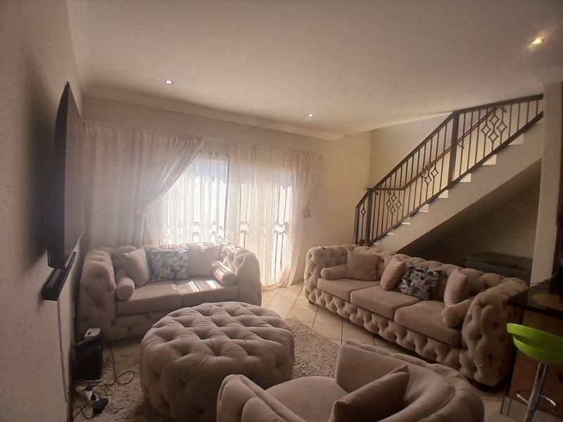 Spacious living room featuring tiled flooring, recessed downlights, and a staircase with a decorative metal balustrade, leading to a bright sliding glass door.