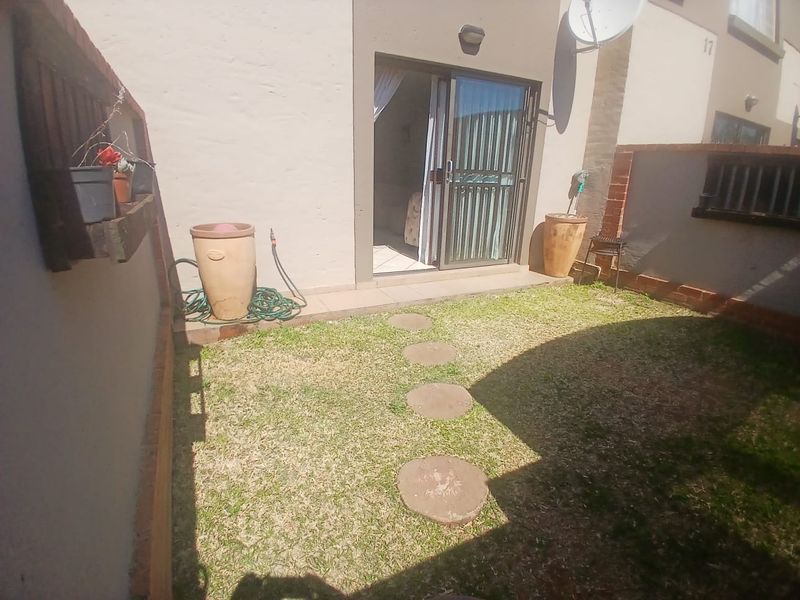 A private rear courtyard featuring a small lawn, stepping stones, and a sliding door providing access to the interior living space.