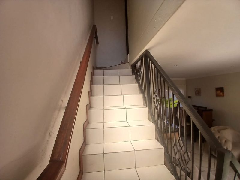 A staircase featuring tiled steps, a wooden handrail, and a decorative metal balustrade leading to the upper level of the townhouse.