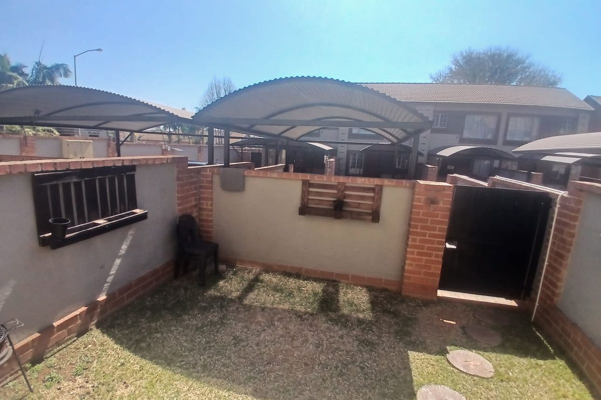 A private rear courtyard area featuring a brick boundary wall, metal gate access, and a curved carport structure providing shade.