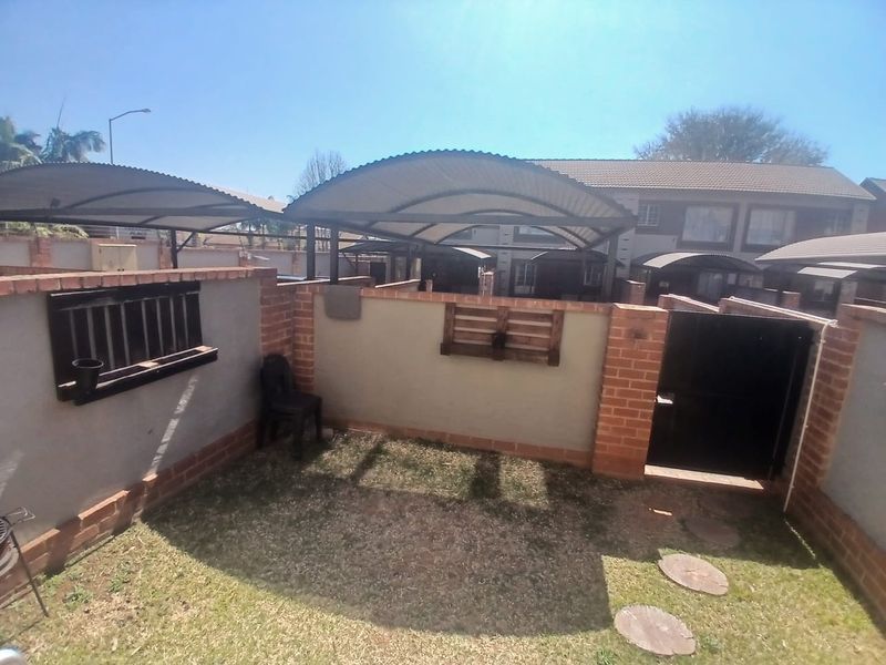 A private rear courtyard area featuring a brick boundary wall, metal gate access, and a curved carport structure providing shade.