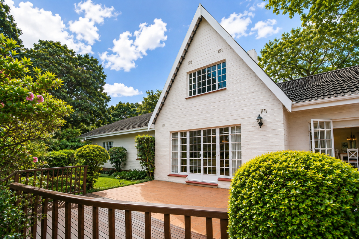 A well-maintained rear exterior view featuring a tiled patio, timber decking, and classic white brick facade with french doors leading to the garden.