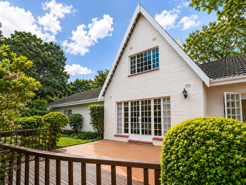 A well-maintained rear exterior view featuring a tiled patio, timber decking, and classic white brick facade with french doors leading to the garden.