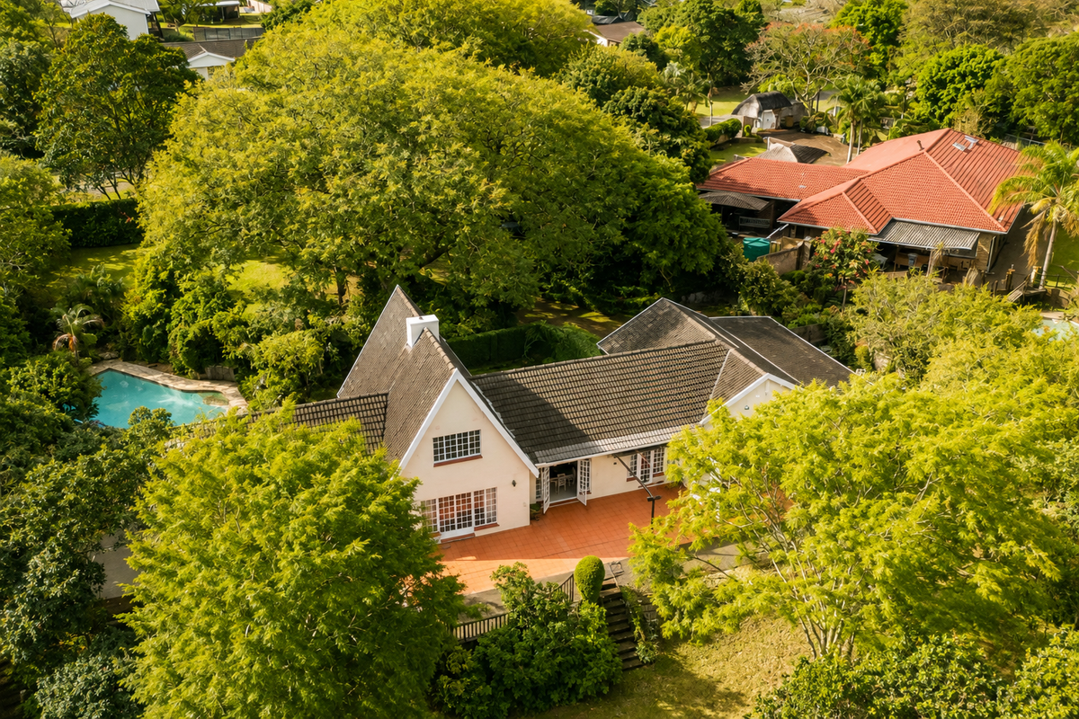 Aerial view of a residential property featuring a tiled roof, a spacious patio area, and a private swimming pool set within a lush garden.