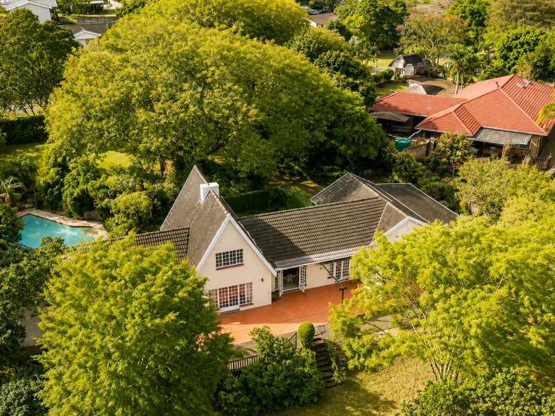 Aerial view of a residential property featuring a tiled roof, a spacious patio area, and a private swimming pool set within a lush garden.