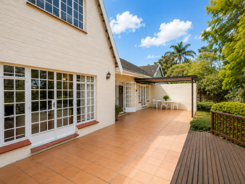 A spacious rear patio featuring terracotta tiling, a timber deck, and a pergola, providing a seamless transition between the indoor living area and the garden.