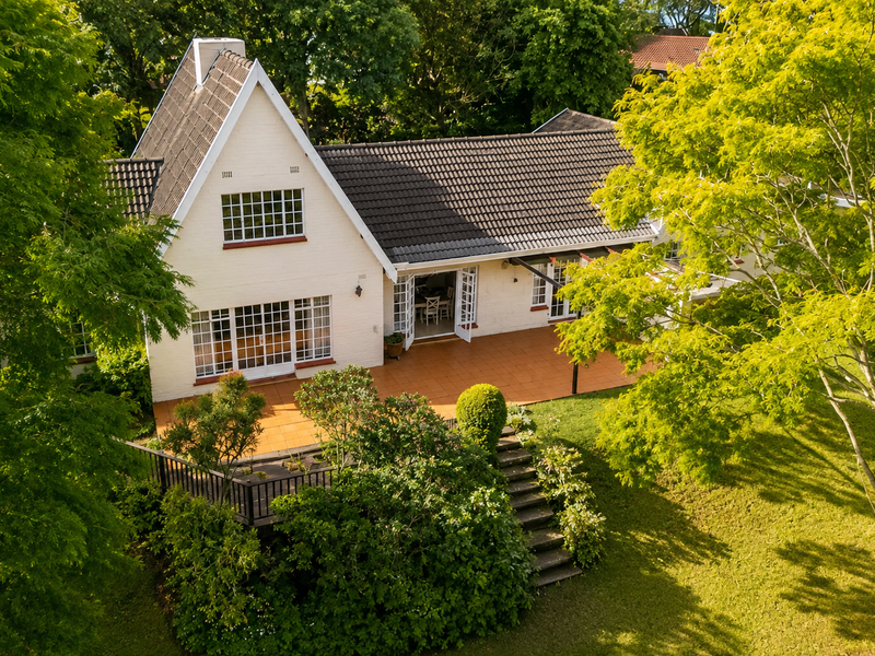 Aerial view of the rear elevation featuring a spacious tiled patio, timber decking, stone steps, and established garden surroundings.