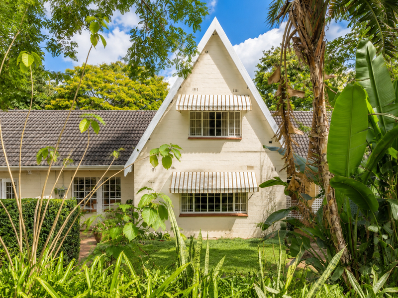 A charming A-frame style rear elevation featuring a pitched roof, concrete tiles, and classic casement windows set within a lush, mature garden.