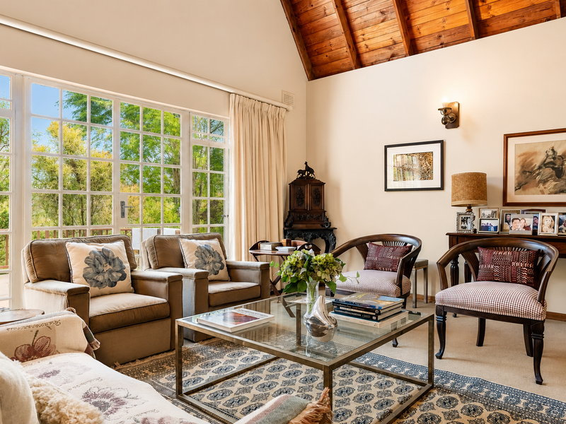 A bright and spacious living room featuring a high vaulted timber ceiling, large windows providing natural light, and neutral carpeted flooring.