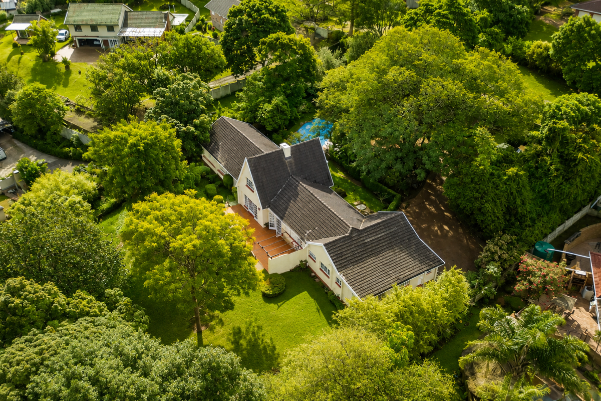 Aerial view of a residential property featuring a tiled roof house, a swimming pool, a paved patio area, and extensive mature garden landscaping.