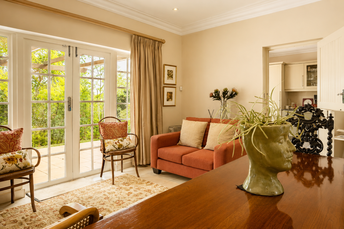 A bright living area featuring classic crown molding, recessed lighting, and double french doors that open onto a paved patio and garden.