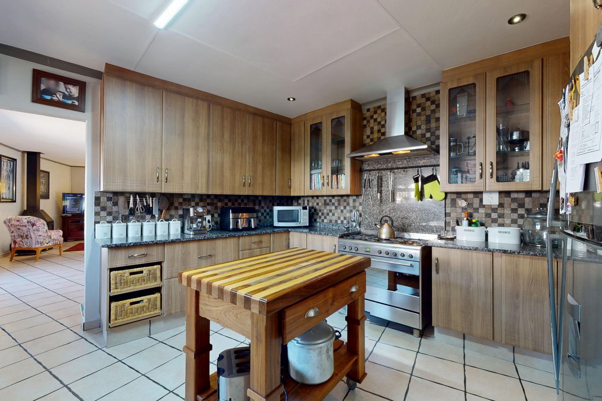 A functional kitchen featuring wood-finish cabinetry, granite countertops, a gas stove with an extractor fan, and tiled flooring.