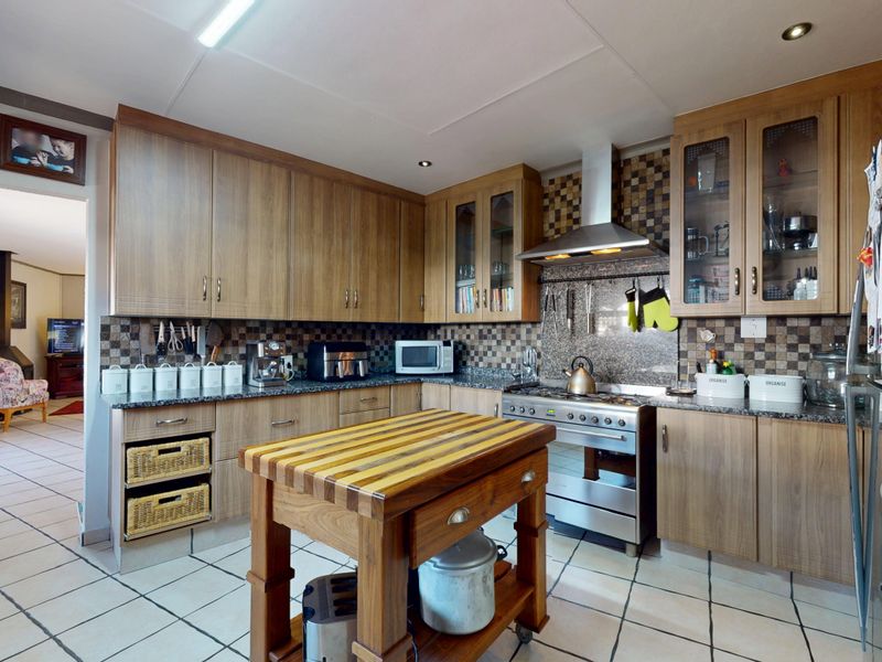 A functional kitchen featuring wood-finish cabinetry, granite countertops, a gas stove with an extractor fan, and tiled flooring.