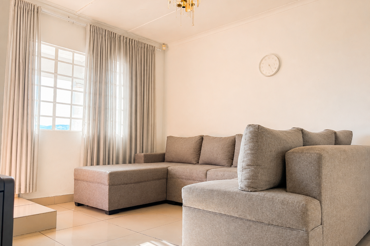 A bright and well-maintained living room featuring neutral tiled flooring, a classic grid-pattern window, and a decorative ceiling light fixture.