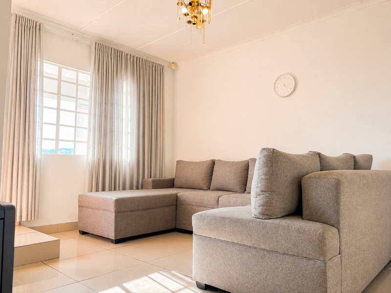A bright and well-maintained living room featuring neutral tiled flooring, a classic grid-pattern window, and a decorative ceiling light fixture.
